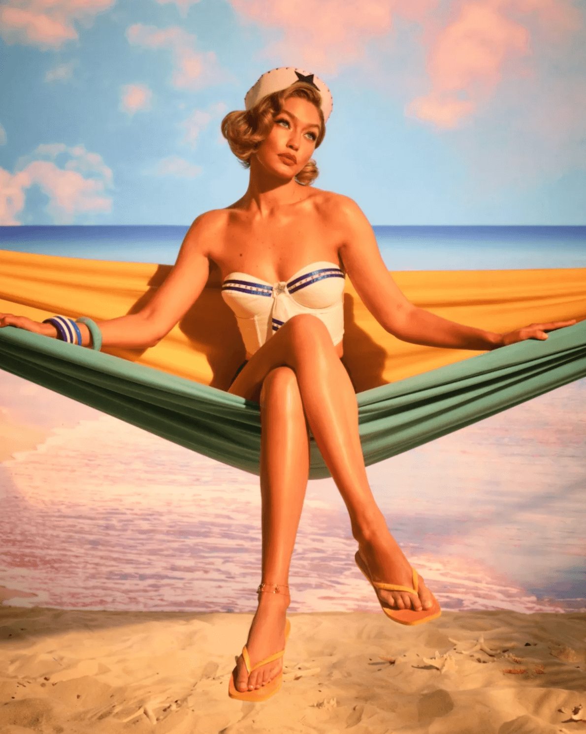 Image shows a vintage poster style image with model Gigi Hadid in a vintage sailor style corset and flip flops. She perches on a hammock with a background representing a beach scene. 