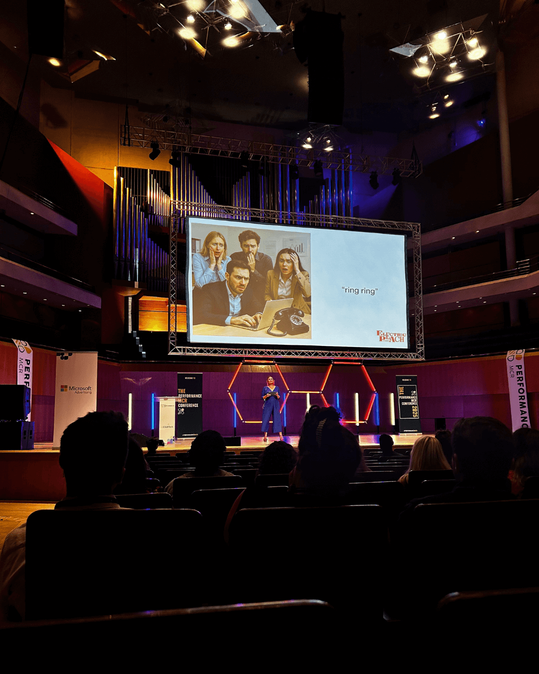 The image shows a marketing expert delivering a talk on AI. The words on screen behind her reads "ring ring" with an image of 4 shocked office workers, and the Electric Peach Studio logo.