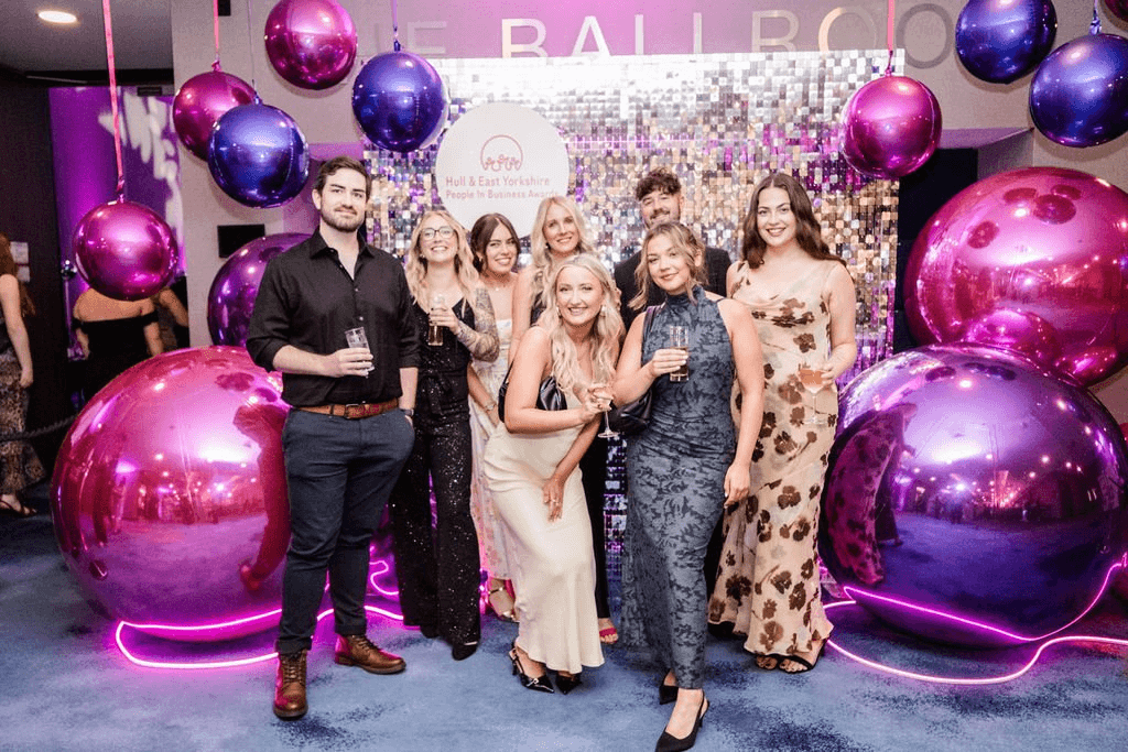 The image shows team Superfly stood in front of an elaborate silver glitterball backdrop with pink & purple balls to the left and right.